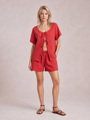 Model stands in a red plaid scoop-neck short-sleeve top with a tied front and matching drawstring shorts in a relaxed silhouette.