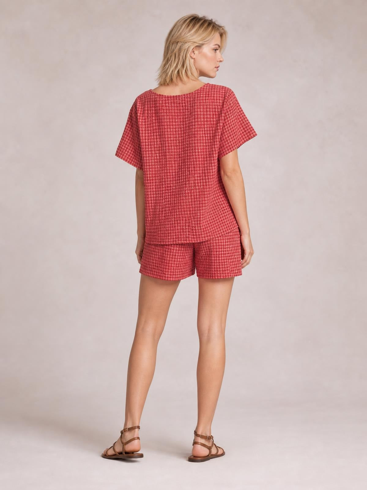 Model turned away wearing a red plaid short-sleeve top with a relaxed silhouette and matching drawstring shorts, showing the back construction and hem.