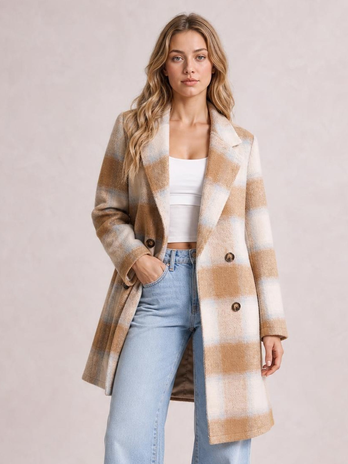 Model poses with one hand in a pocket wearing a beige and cream plaid longline jacket with notched lapels, buttons, and a relaxed silhouette.
