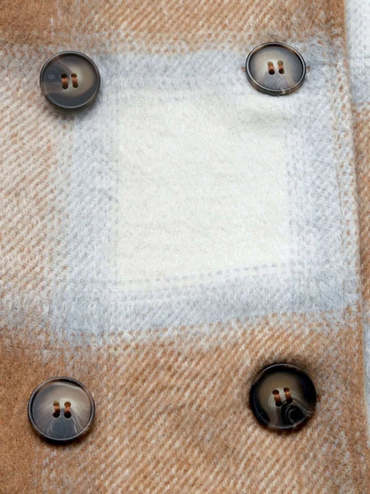 Close-up of a tan and gray plaid longline jacket fabric featuring a soft textured weave and four dark two-hole buttons.