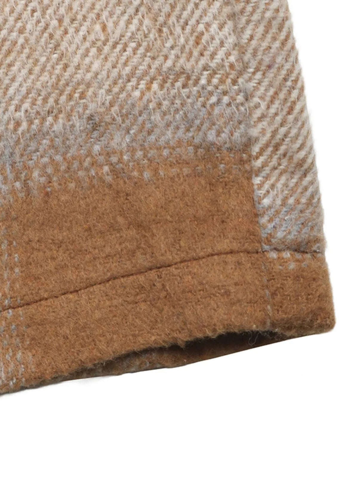 Close-up of the brown and tan plaid longline jacket fabric, showing its textured weave, stitched seam, and neatly finished lower edge.