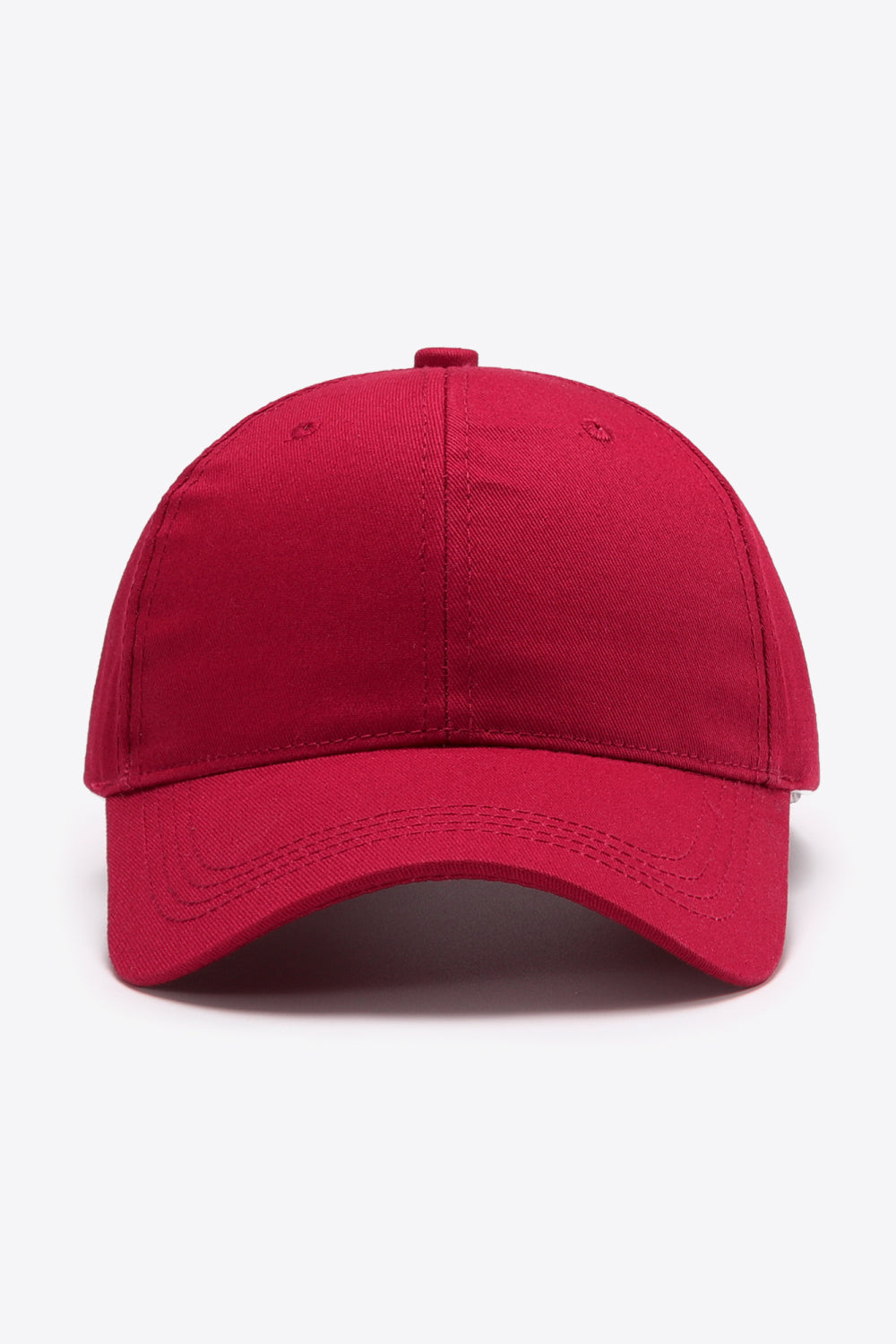 A solid red cotton baseball cap features a structured six-panel crown, gently curved brim, tonal stitching, and subtle ventilation eyelets.