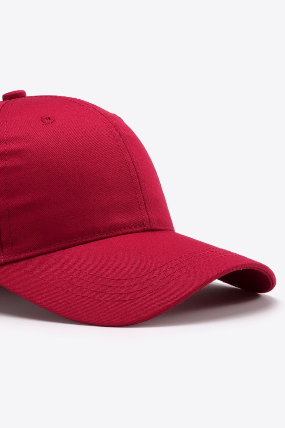 Solid burgundy cotton baseball cap with a structured six-panel crown, gently curved brim, tonal stitching, and a small ventilation eyelet.