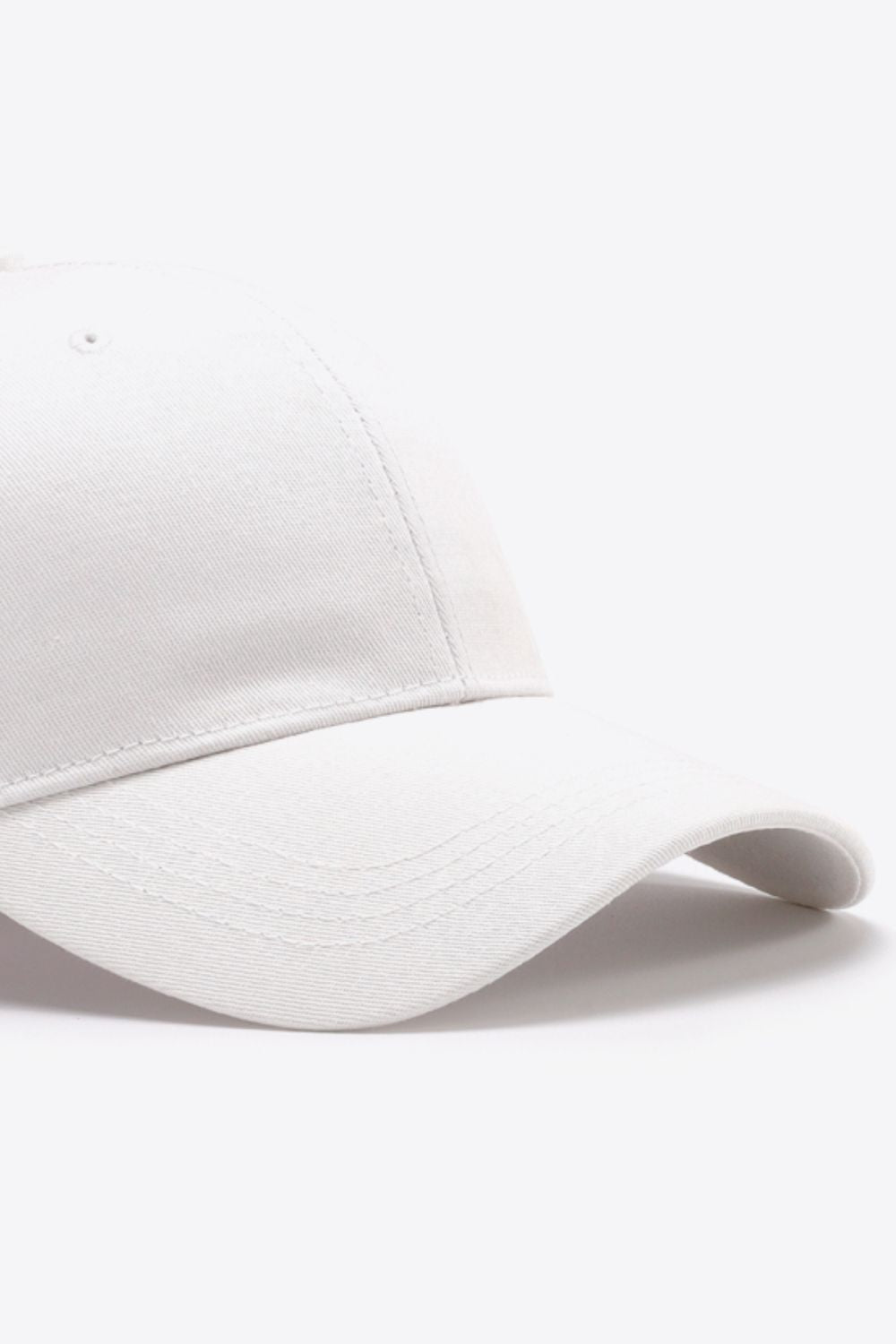 Plain white cotton baseball cap shown in close-up with a structured six-panel crown, gently curved brim, tonal stitching, and a ventilation eyelet.