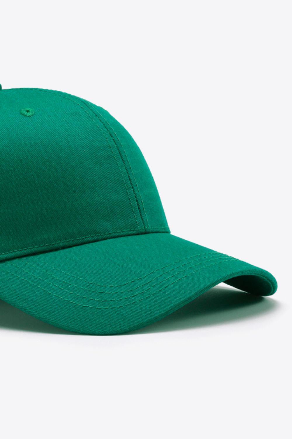 A plain green cotton baseball cap with a structured six-panel-inspired crown, curved brim, tonal stitching, and a small ventilation eyelet.