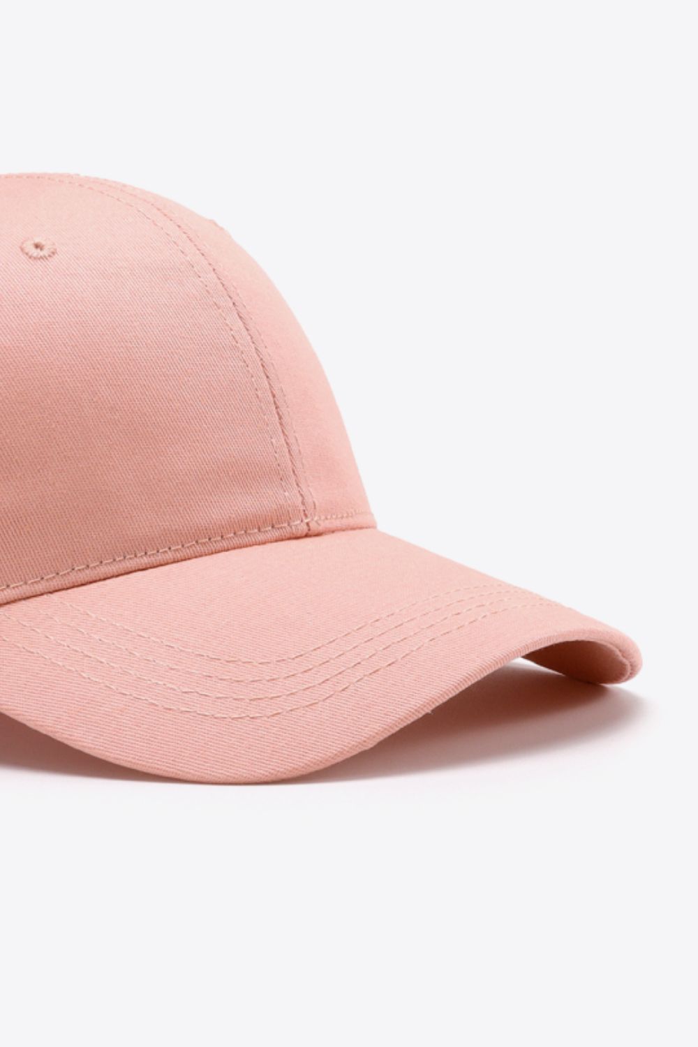 A solid pink cotton baseball cap with a structured six-panel crown, curved brim, tonal stitching, and a small ventilation eyelet.