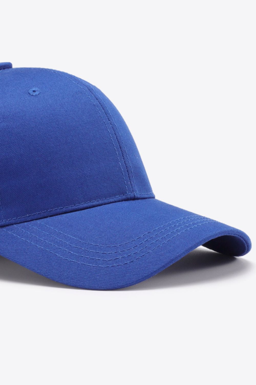 Solid blue cotton baseball cap with a structured six-panel crown, gently curved brim, tonal stitching, and a small ventilation eyelet.