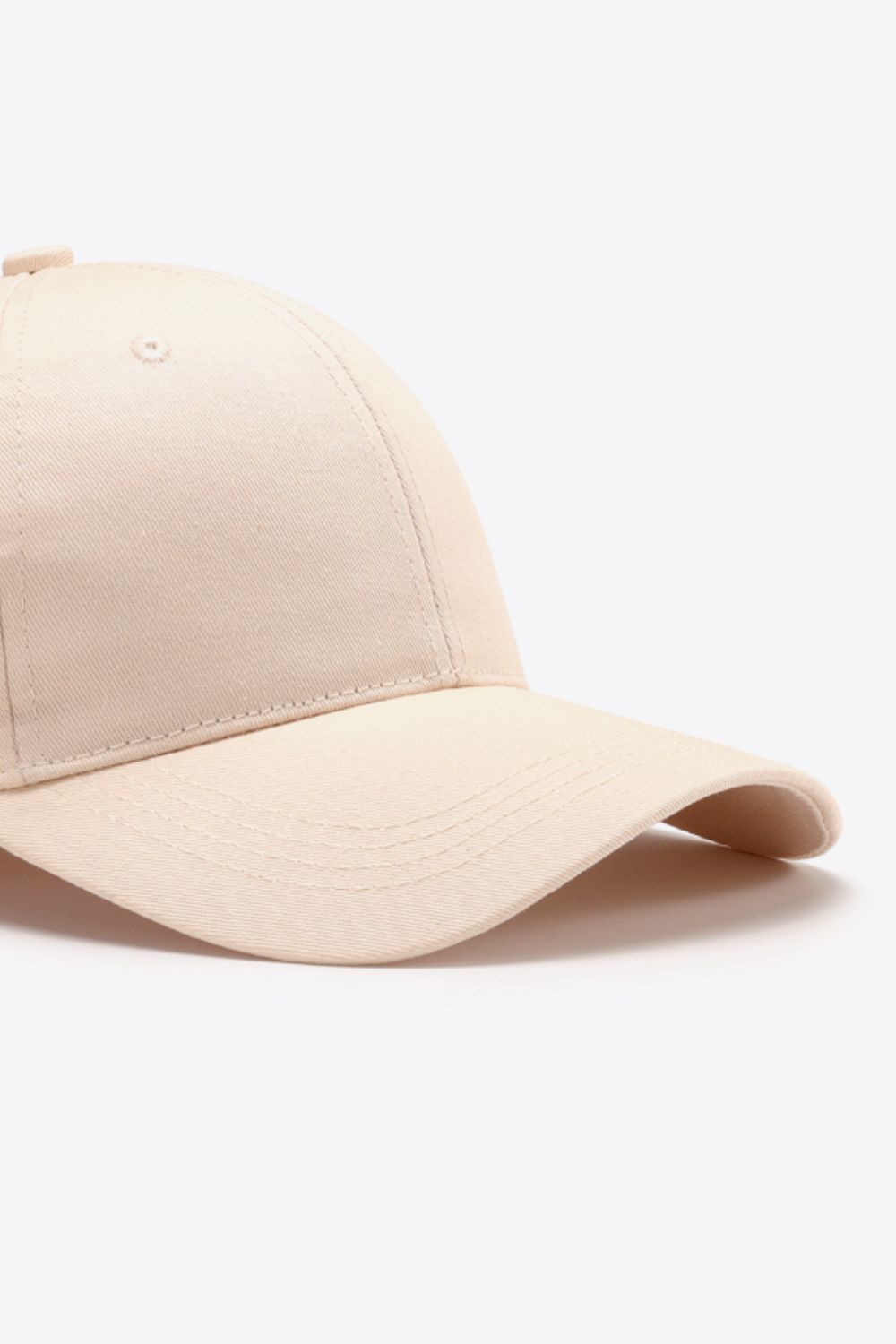 A plain beige cotton baseball cap with a structured six-panel crown, tonal stitching, ventilation eyelet, and gently curved brim.