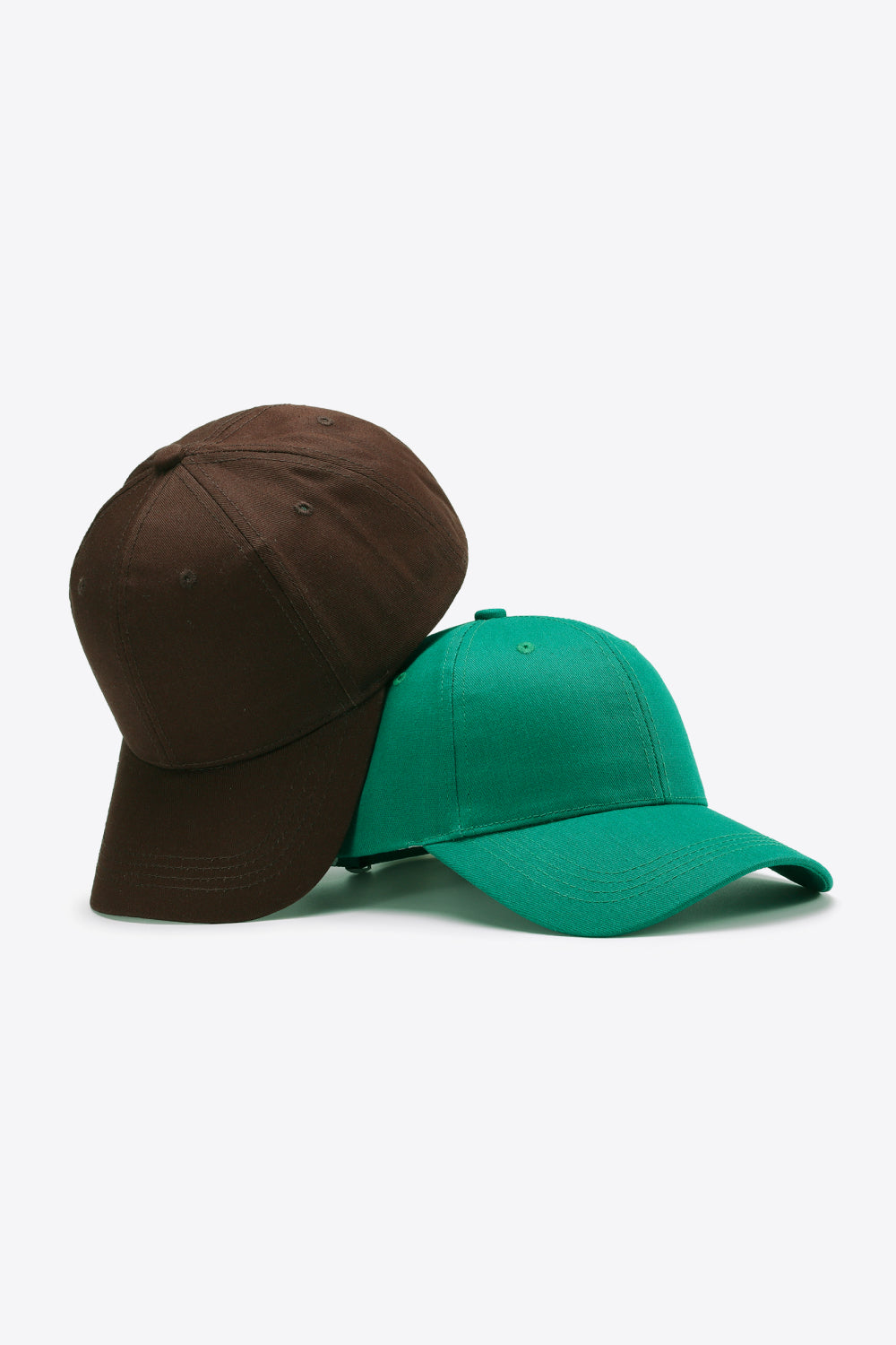 Two plain cotton baseball caps in brown and teal feature structured six-panel crowns, curved brims, tonal stitching, and ventilation eyelets.