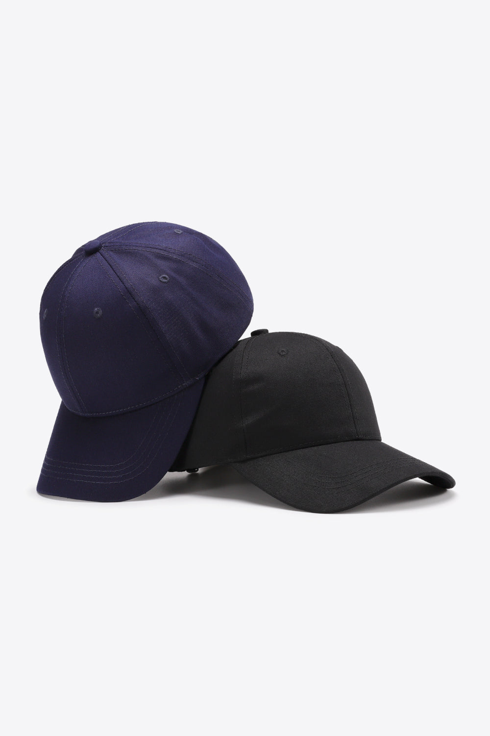 Two plain cotton baseball caps in navy and black feature structured six-panel crowns, curved brims, tonal stitching, and small ventilation eyelets.