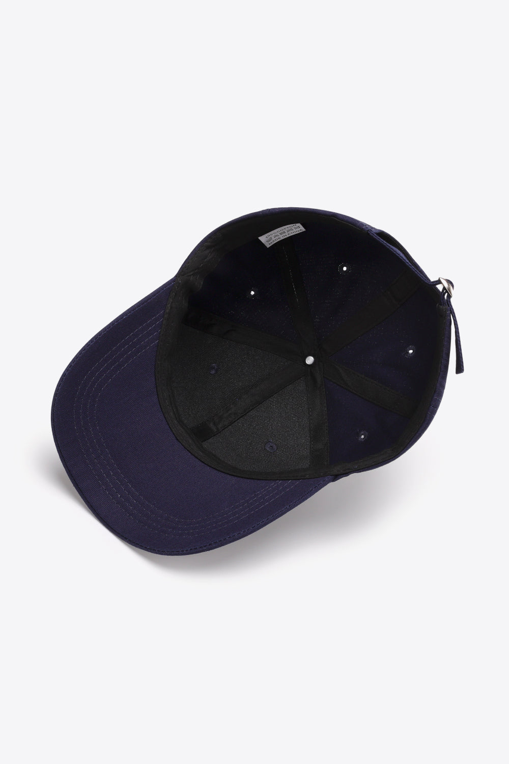 A solid navy cotton baseball cap is shown from underneath, highlighting its six-panel construction, curved brim, tonal stitching, ventilation eyelets, and adjustable metal-buckle strap.