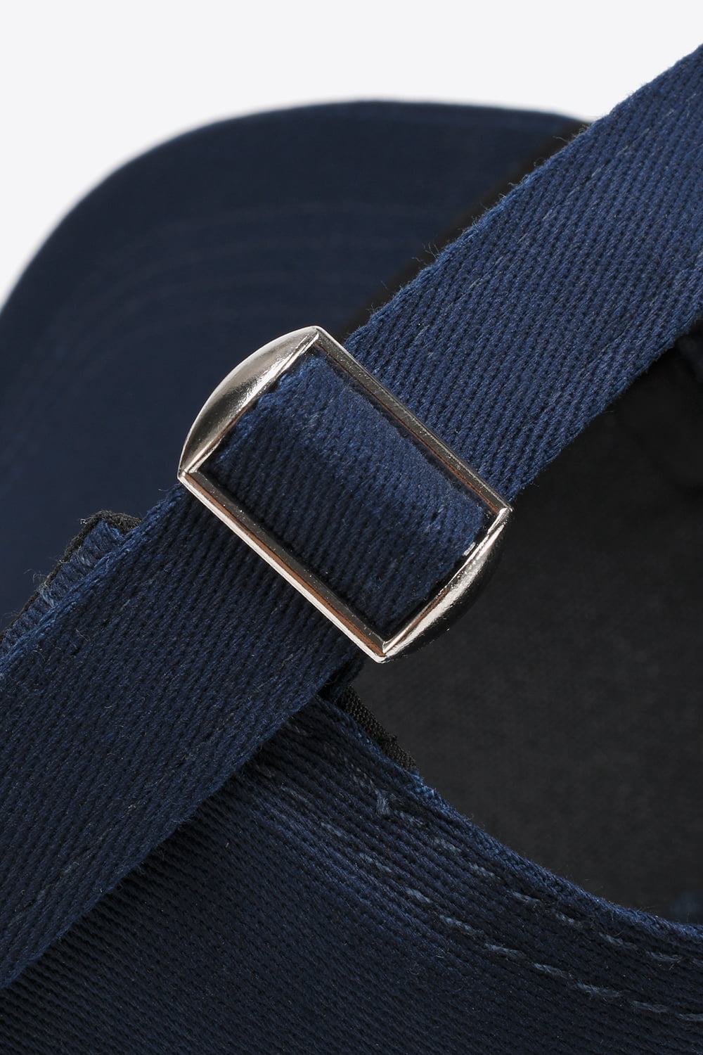 Close-up of a solid navy cotton baseball cap showing its textured adjustable back strap and polished metal buckle construction.