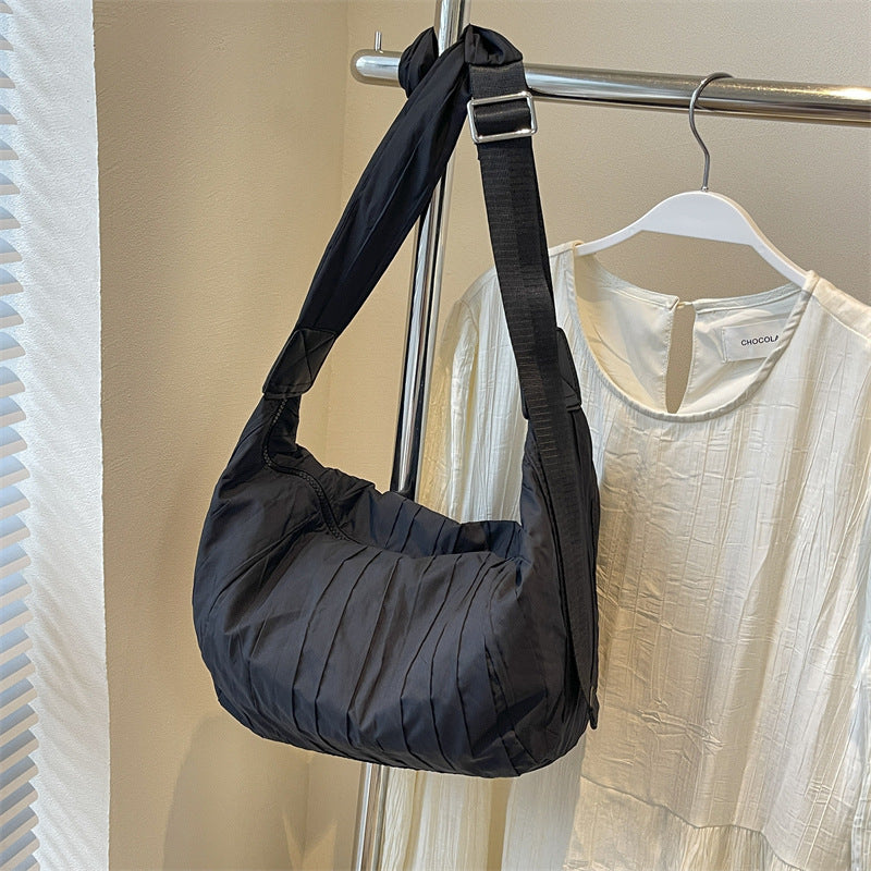 Black Pleated Dumpling Crossbody Bag with a soft, slouchy crescent silhouette, gathered pleats, and a broad adjustable shoulder strap.