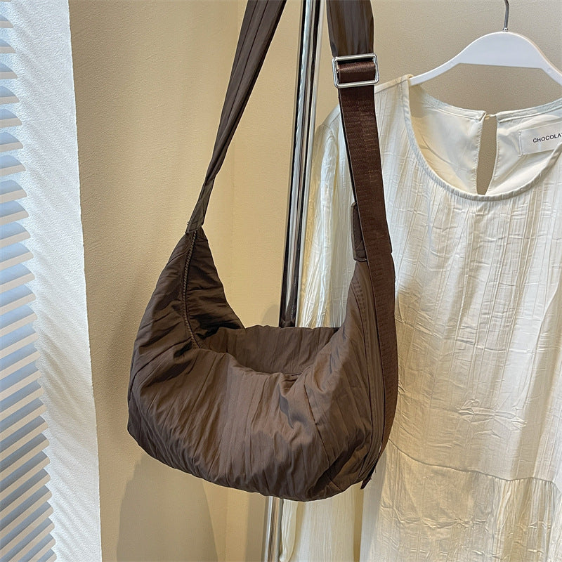 Brown Pleated Dumpling Crossbody Bag with a softly sculpted crescent silhouette, gathered pleats, slouchy construction, and a broad adjustable strap.