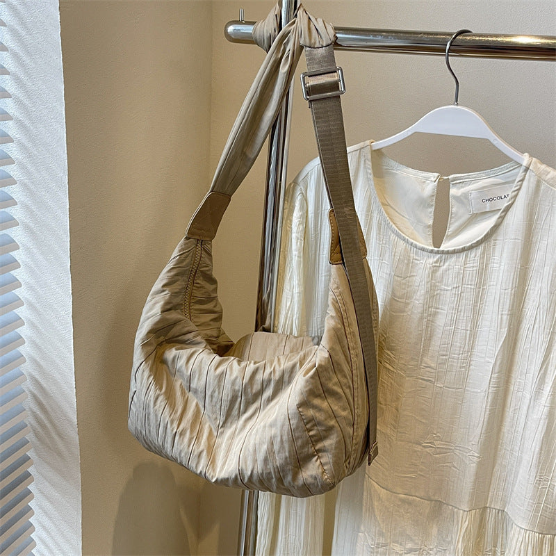 A medium taupe Pleated Dumpling Crossbody Bag with a soft crescent silhouette, gathered pleats, slouchy construction, and a broad adjustable shoulder strap.
