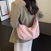 A model wears the pink Pleated Dumpling Crossbody Bag over one shoulder, showing its soft crescent silhouette, gathered pleats, slouchy shape, and broad strap.