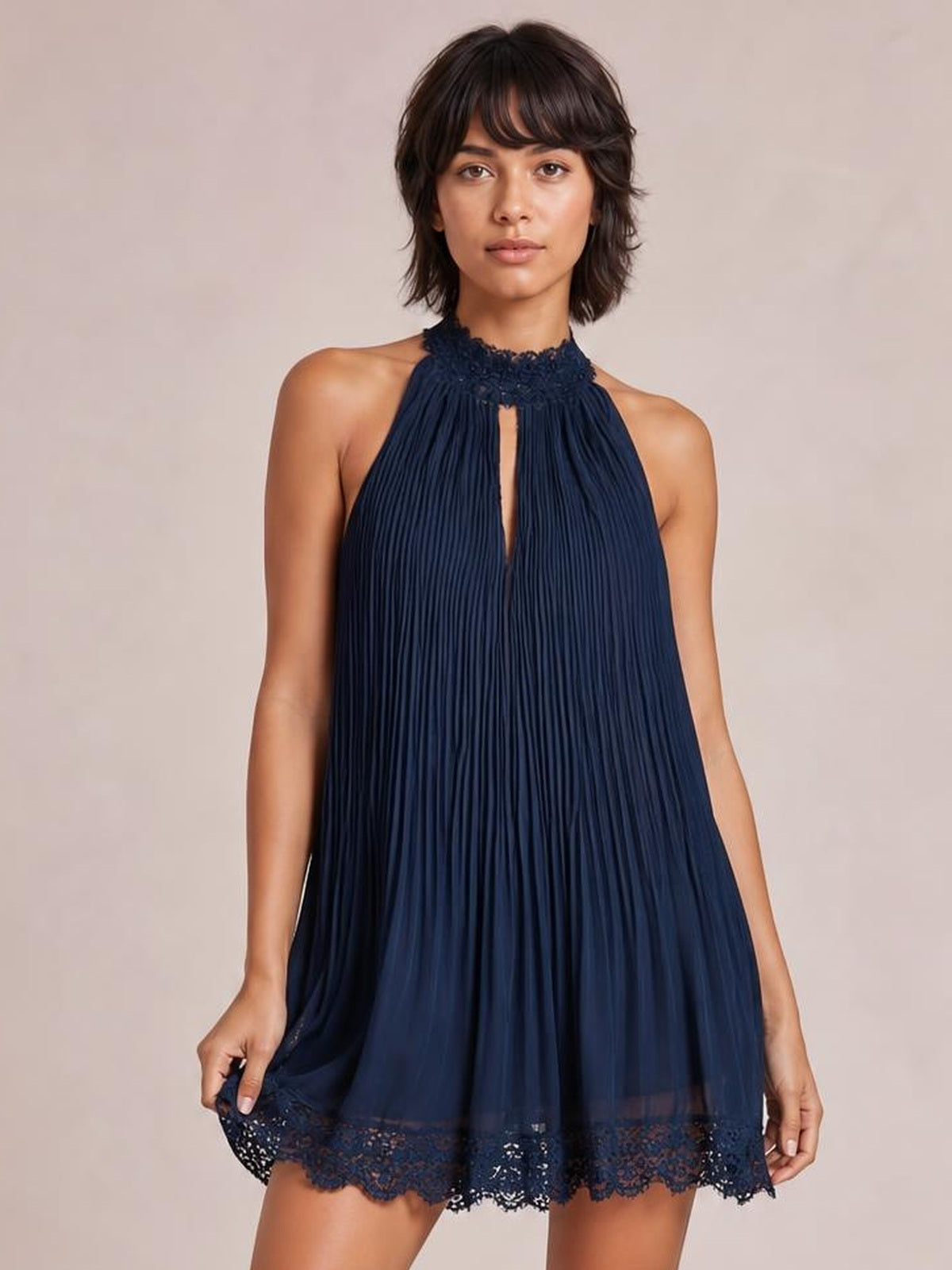 Model holds the hem of a navy pleated lace-trim sleeveless mini dress with a relaxed A-line silhouette, high neckline, and front cutout.