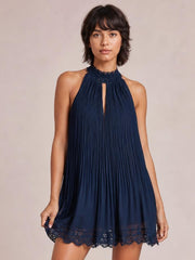 Model holds the hem of a navy pleated lace-trim sleeveless mini dress with a relaxed A-line silhouette, high neckline, and front cutout.