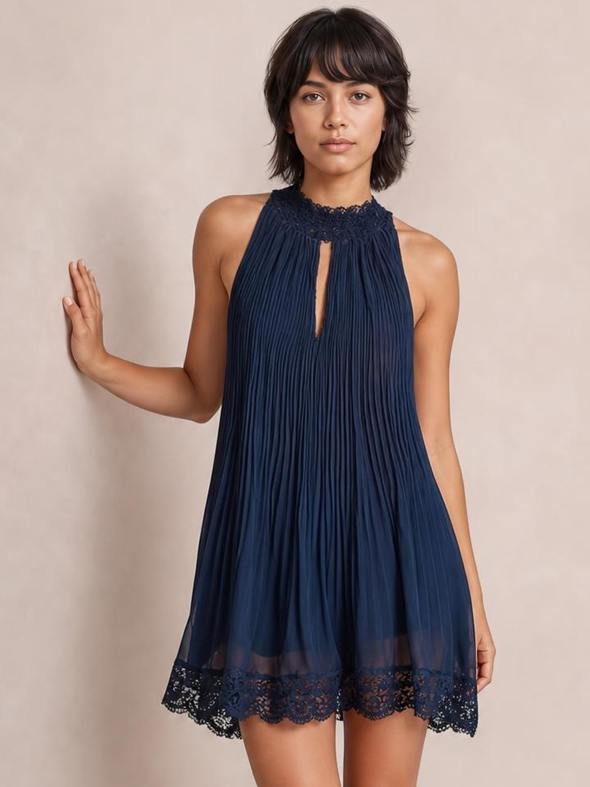 Model wearing a navy sleeveless mini dress with fine pleats, lace-trimmed neckline and hem, a front keyhole cutout, and a relaxed A-line silhouette.