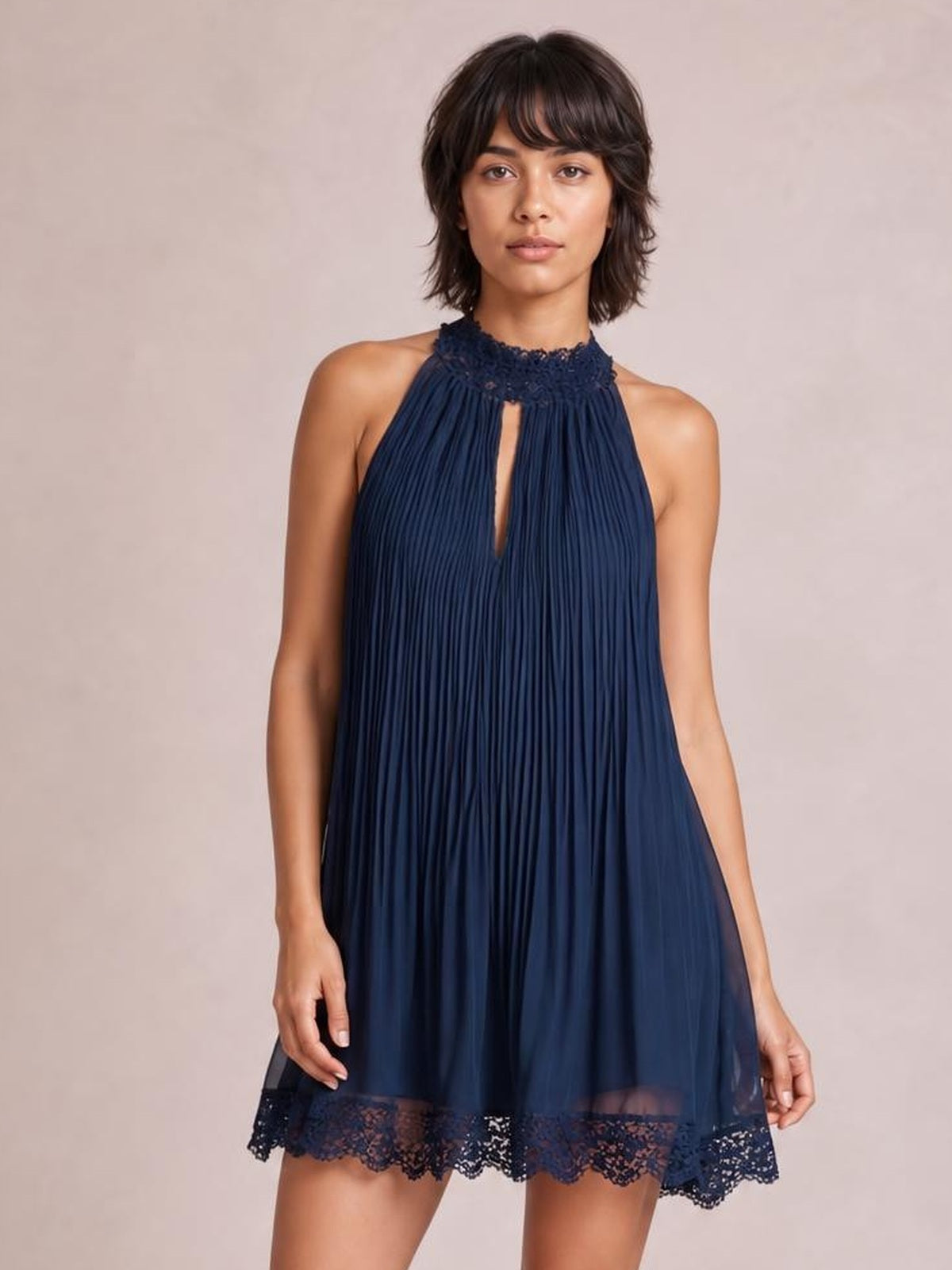 A model stands in a navy sleeveless mini dress with fine pleats, a high lace-trimmed neckline, front cutout, and flowing A-line silhouette.