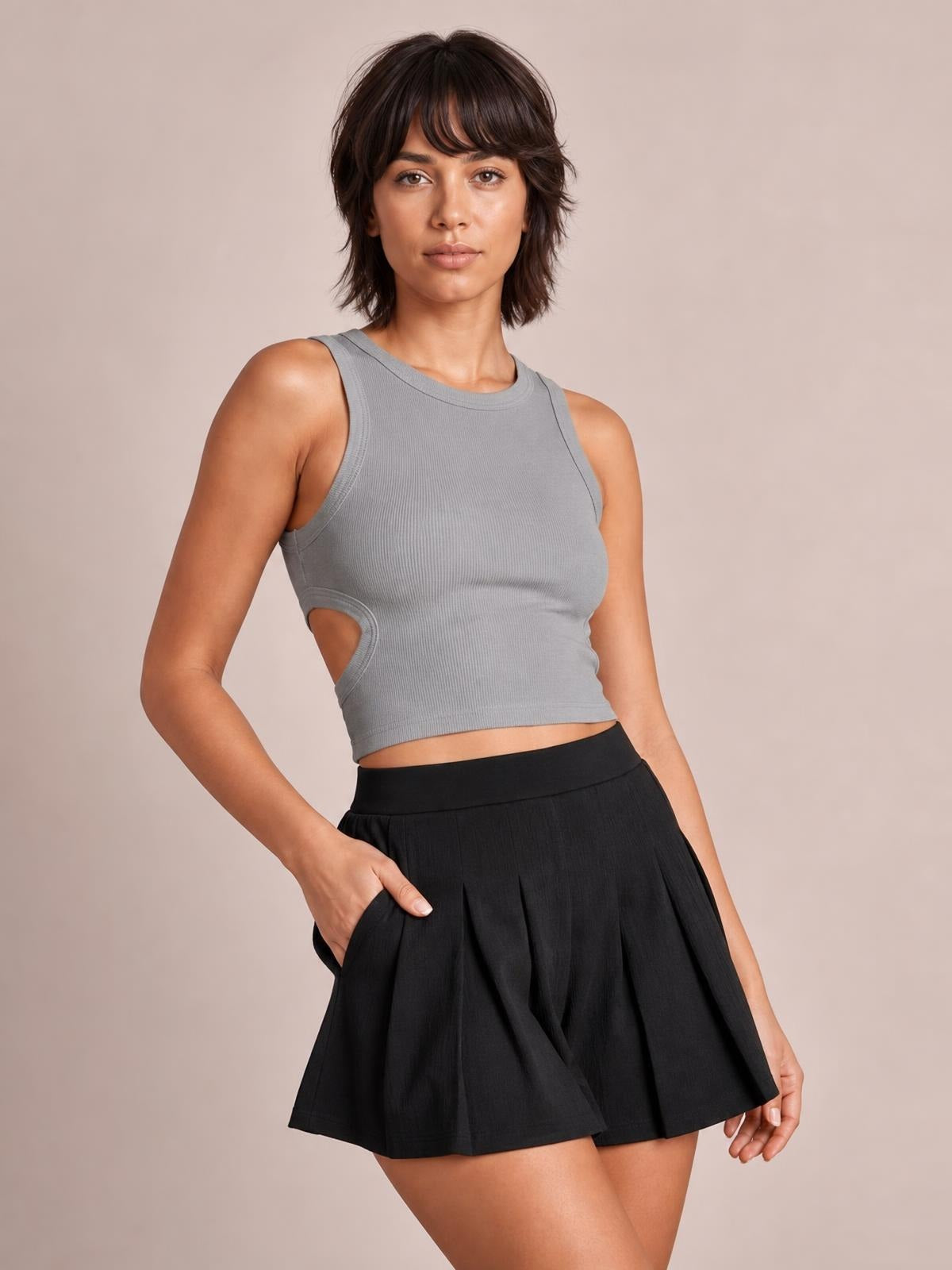 Model wearing black pleated shorts with pockets, a high waistband, and a relaxed flared silhouette, posing with one hand tucked into a pocket.