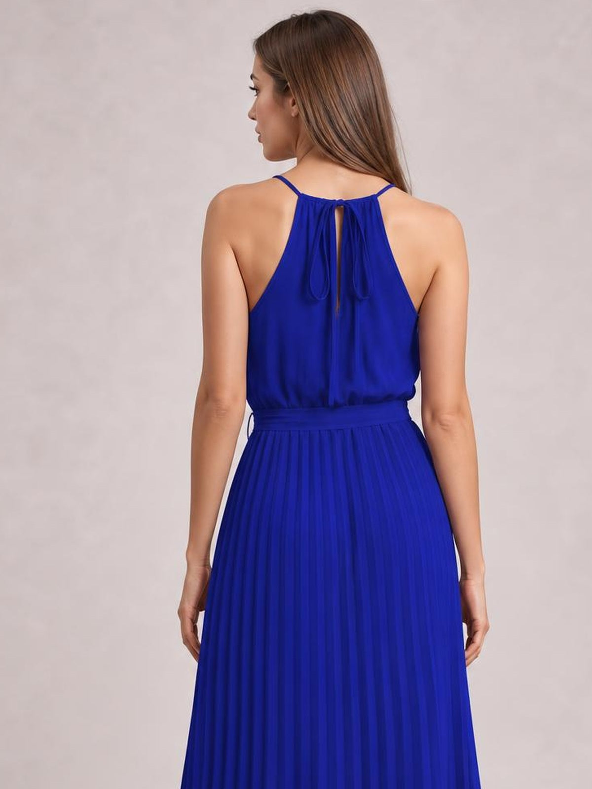 A model stands facing away in a royal blue pleated spaghetti strap midi dress with a tied waist, gathered back neckline, and flowing A-line silhouette.