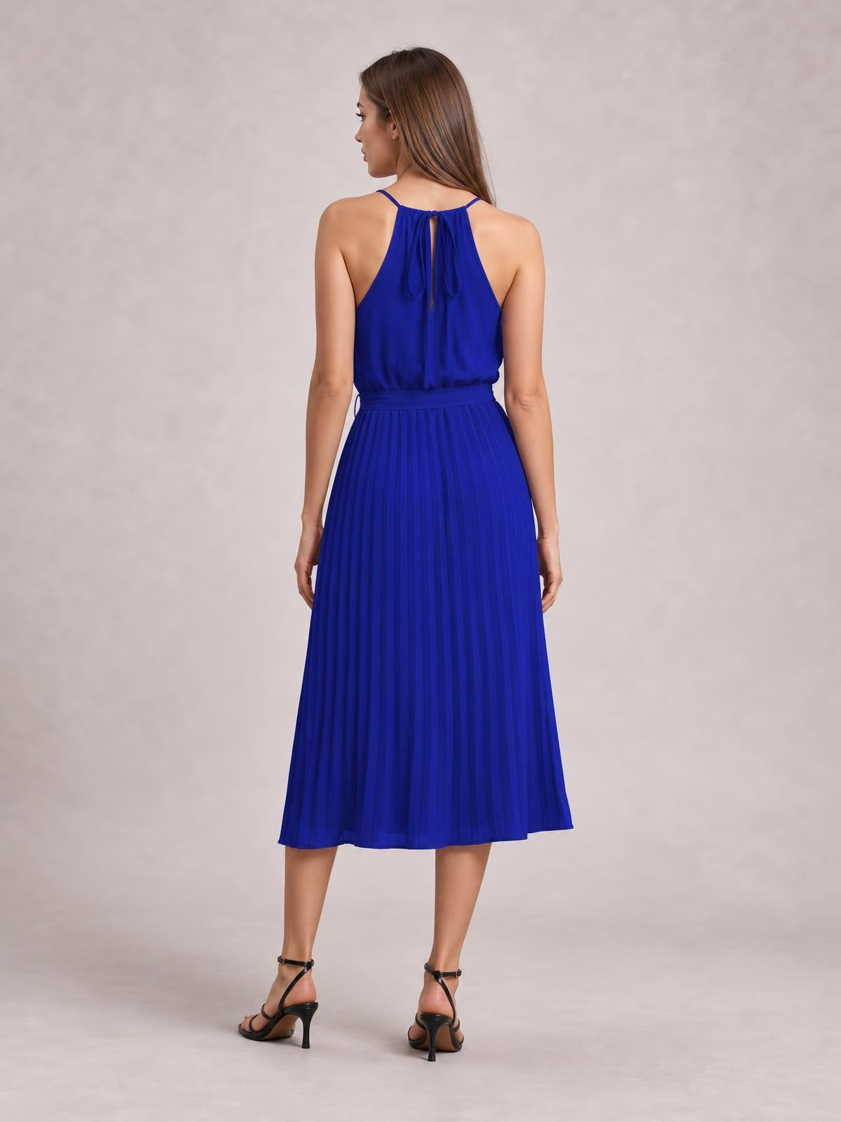A model stands with her back to the camera in a royal blue pleated spaghetti-strap midi dress with a defined tie waist and flowing A-line silhouette.