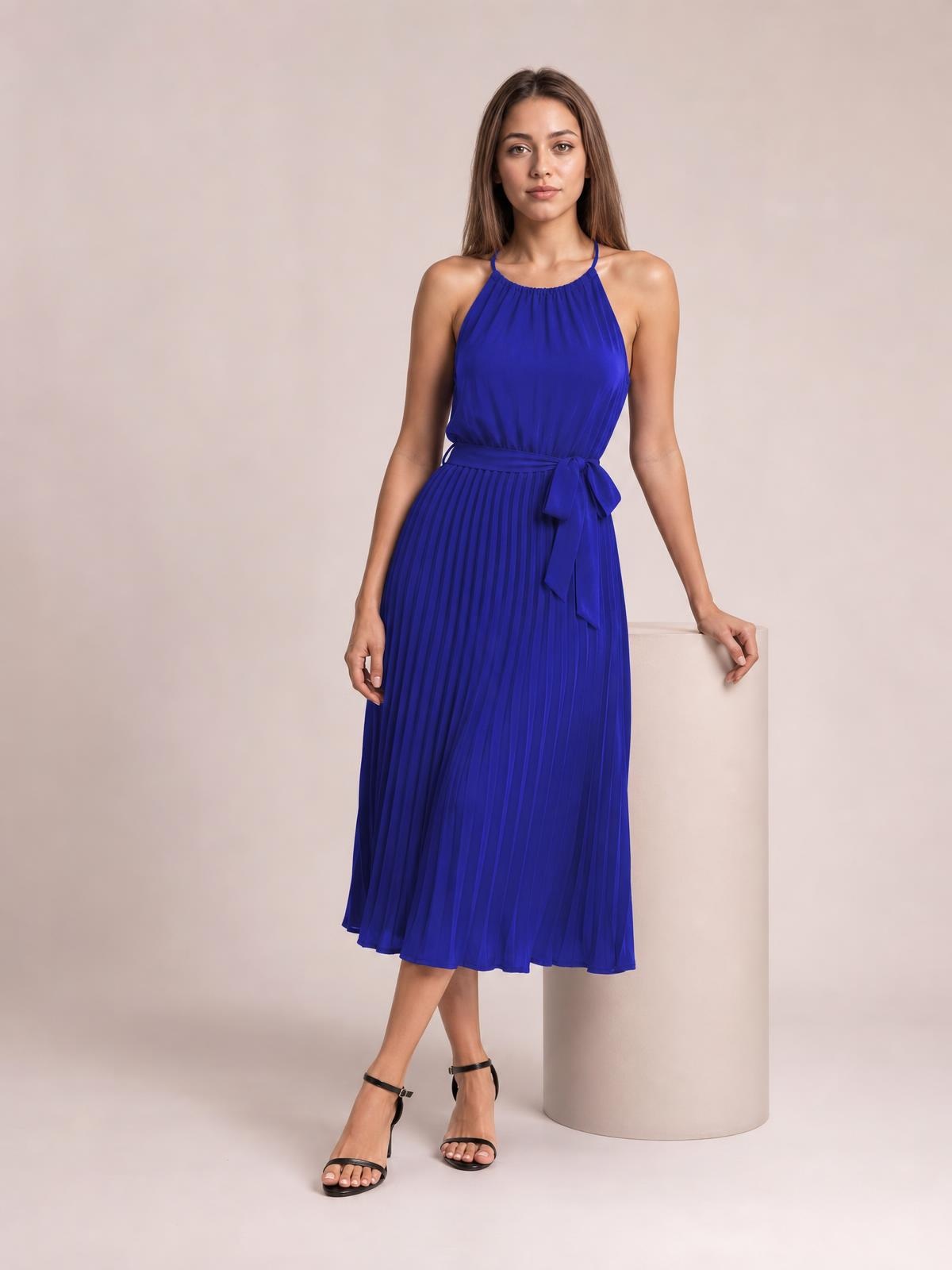 A model wears a royal blue pleated spaghetti strap midi dress with a tied waist bow, flowing A-line silhouette, and strappy black sandals.