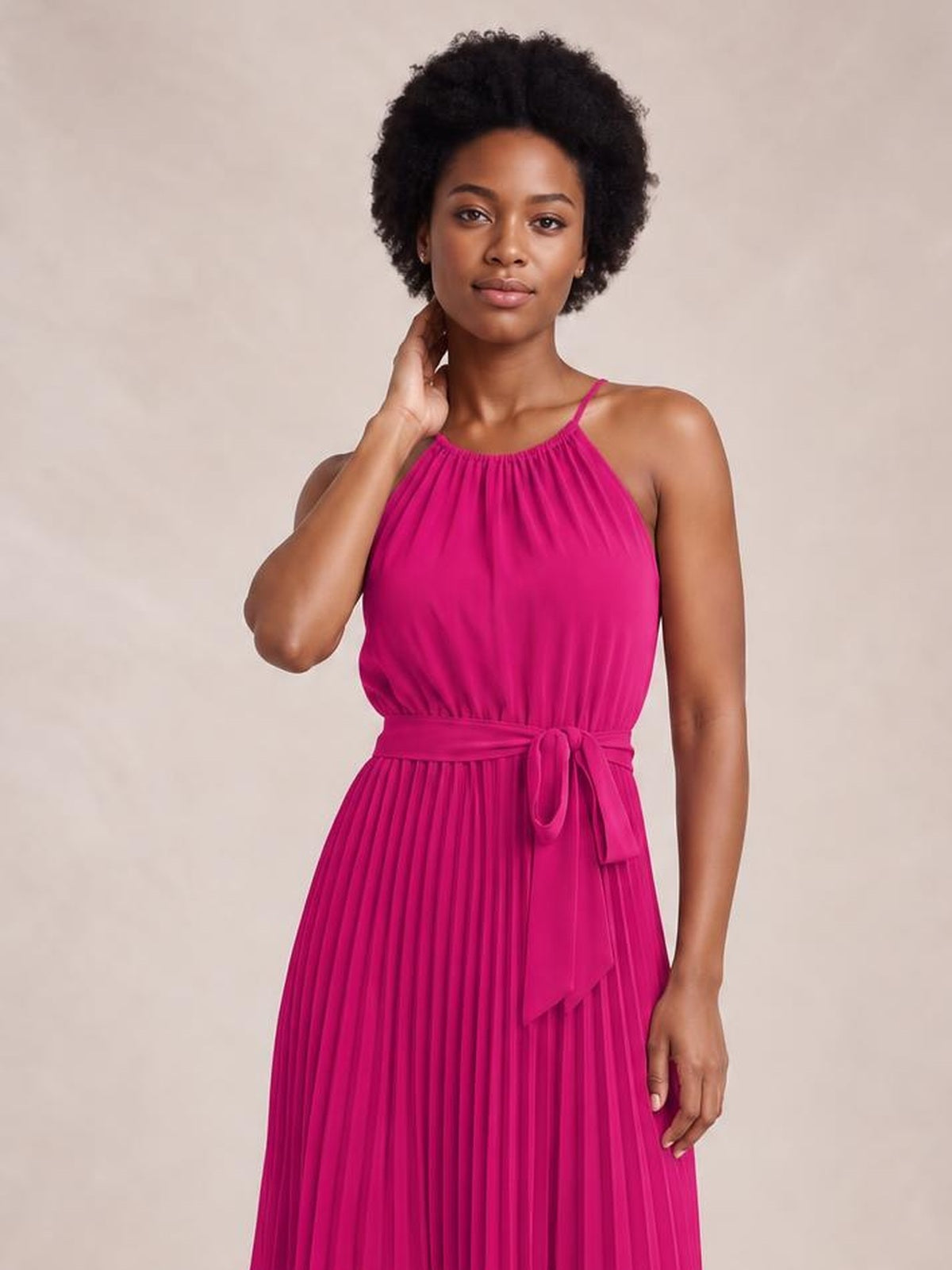 Model wearing a vivid magenta pleated spaghetti strap midi dress with a gathered neckline, flowing silhouette, and tied waist detail.