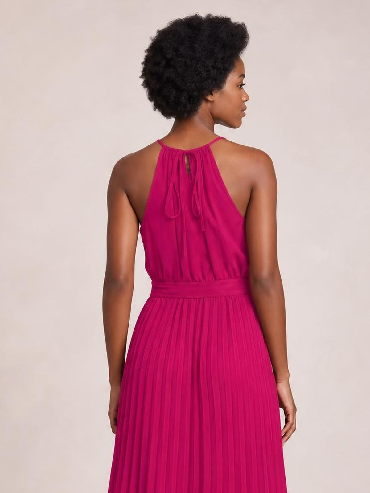 Model shown from the back in a vivid magenta pleated spaghetti strap midi dress with a defined tie waist, flowing A-line silhouette, and back neckline ties.