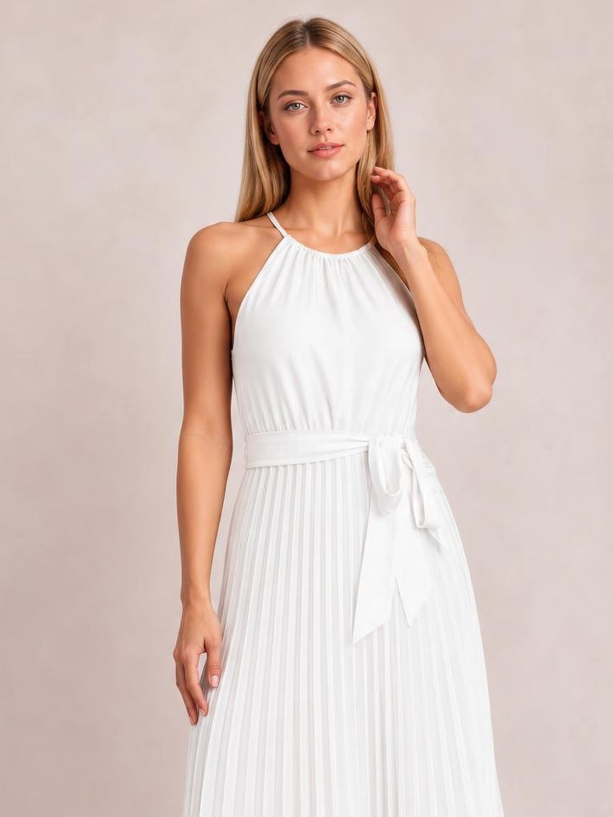 Model poses in a white pleated midi dress with spaghetti straps, a fitted bodice, flowing silhouette, and tied waist belt.