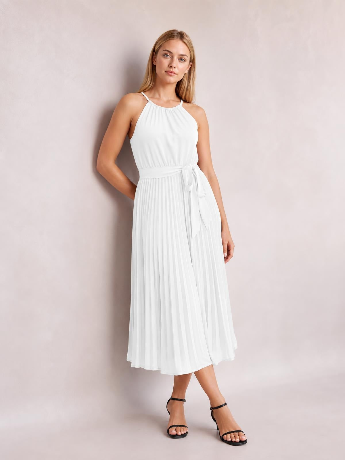 Model poses in a white pleated midi dress with spaghetti straps, a gathered neckline, tied waist, and flowing A-line silhouette, with one hand behind her back.