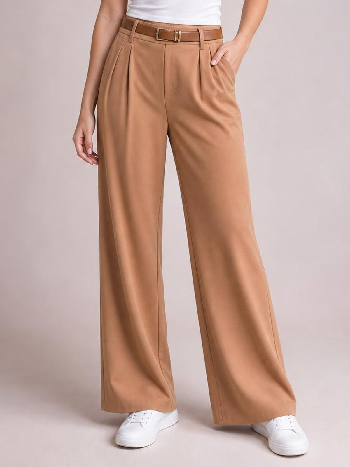 Model wearing camel pleated wide leg pants with a belted waistband, front pockets, tailored seams, and a relaxed full-length silhouette.