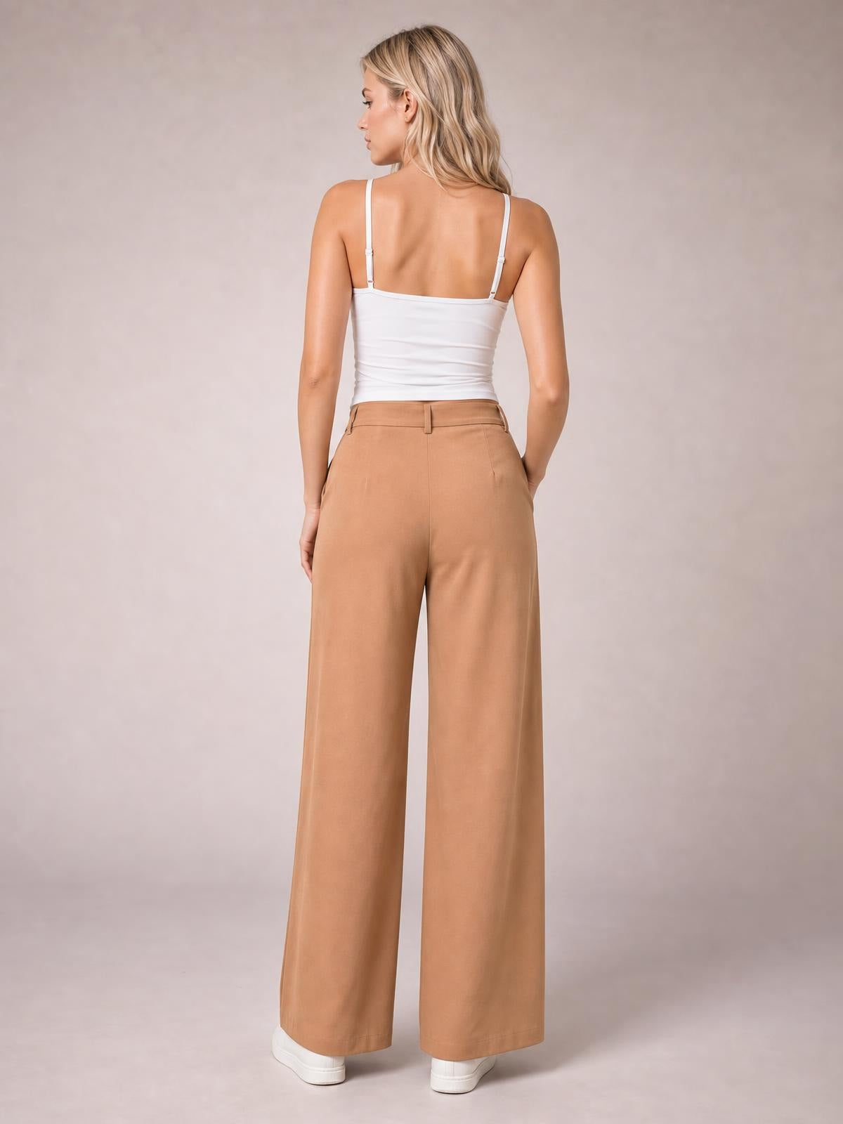 Model shown from behind wearing camel pleated wide-leg pants with a structured waistband, belt loops, side pockets, and full-length silhouette.