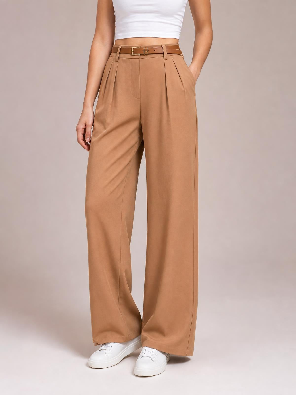 Model wearing camel pleated wide leg pants with a high waist, belt loops, front pockets, and tailored pleats, standing in white sneakers.