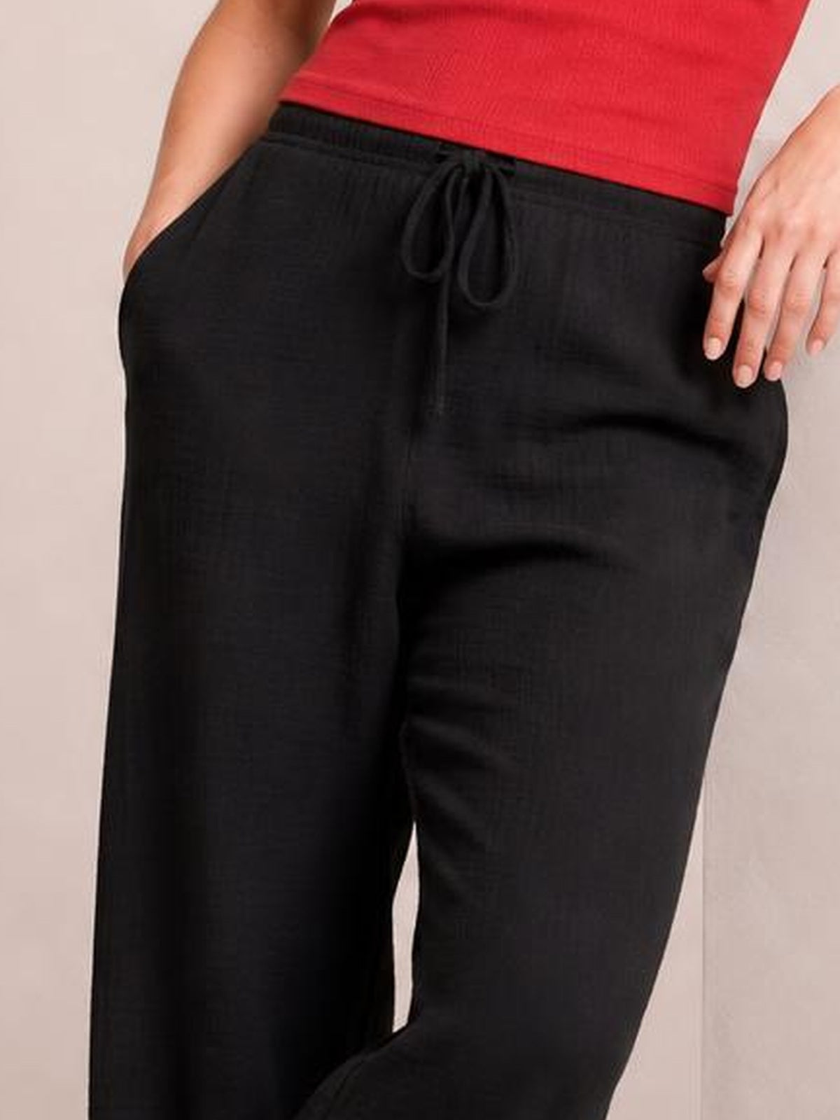 A visible model wears black drawstring jogger pants with a relaxed, loose silhouette, elastic waistband, tied front cord, and side pockets.