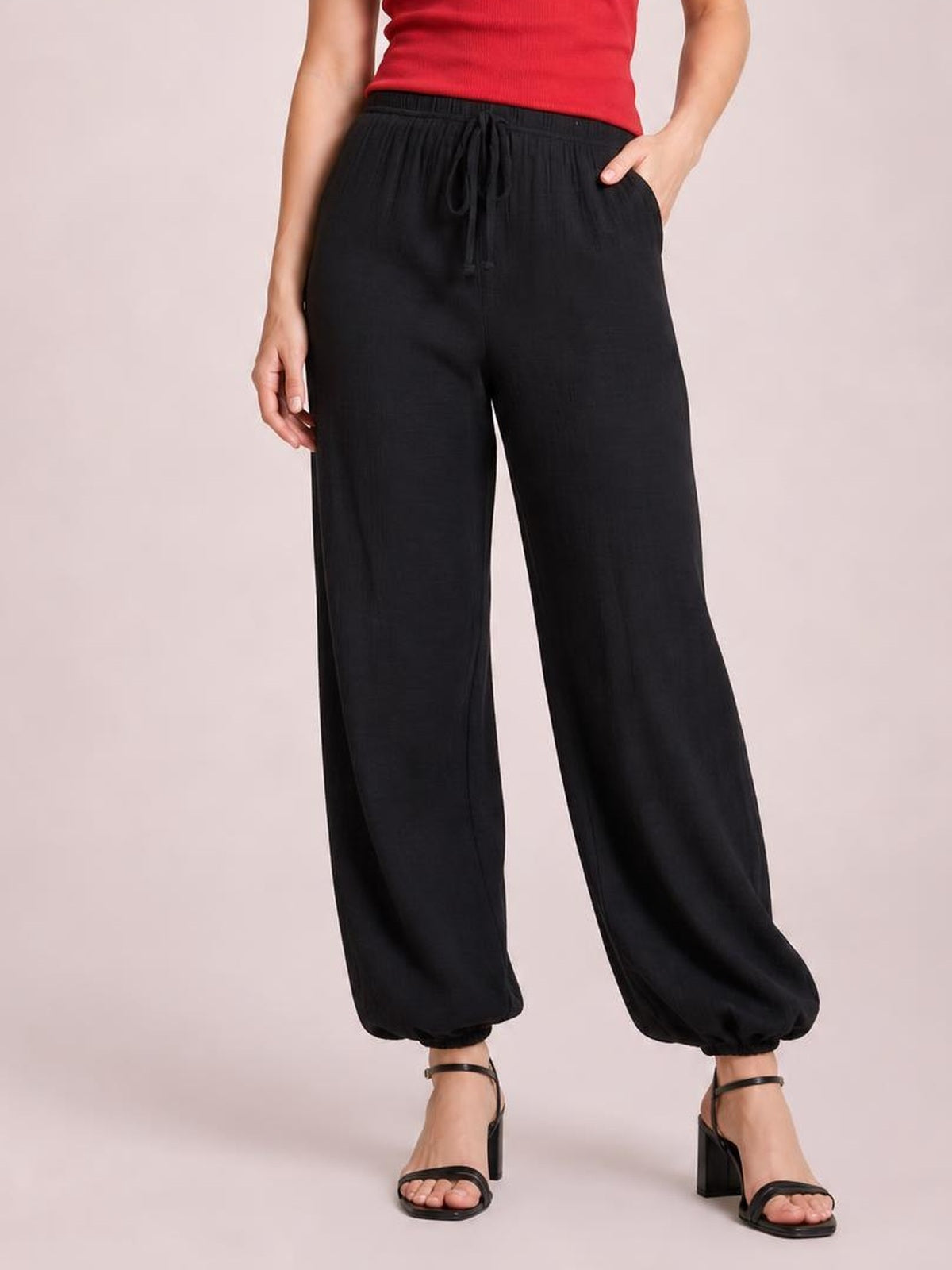 Model wears black drawstring jogger pants with a relaxed, wide-leg silhouette, elasticized cuffs, and hands in the side pockets.