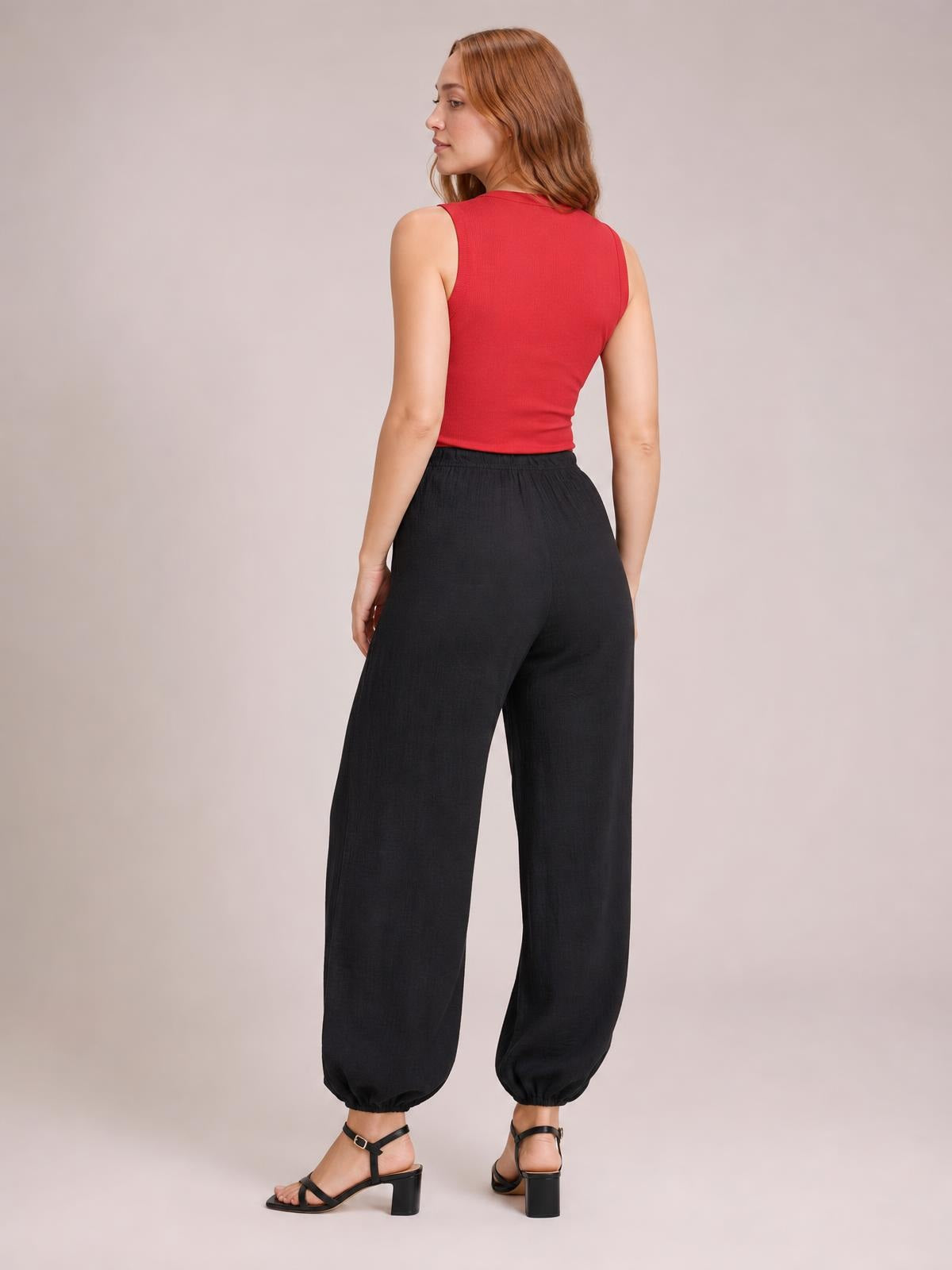 A model poses in a rear three-quarter view wearing black drawstring jogger pants with a relaxed, loose silhouette, elastic waistband, and gathered ankle cuffs.