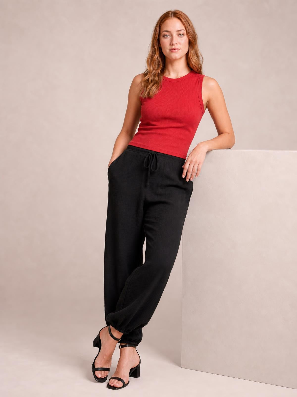 Model poses in black drawstring jogger pants with a relaxed silhouette, tied waist, roomy legs, and gathered ankle cuffs.