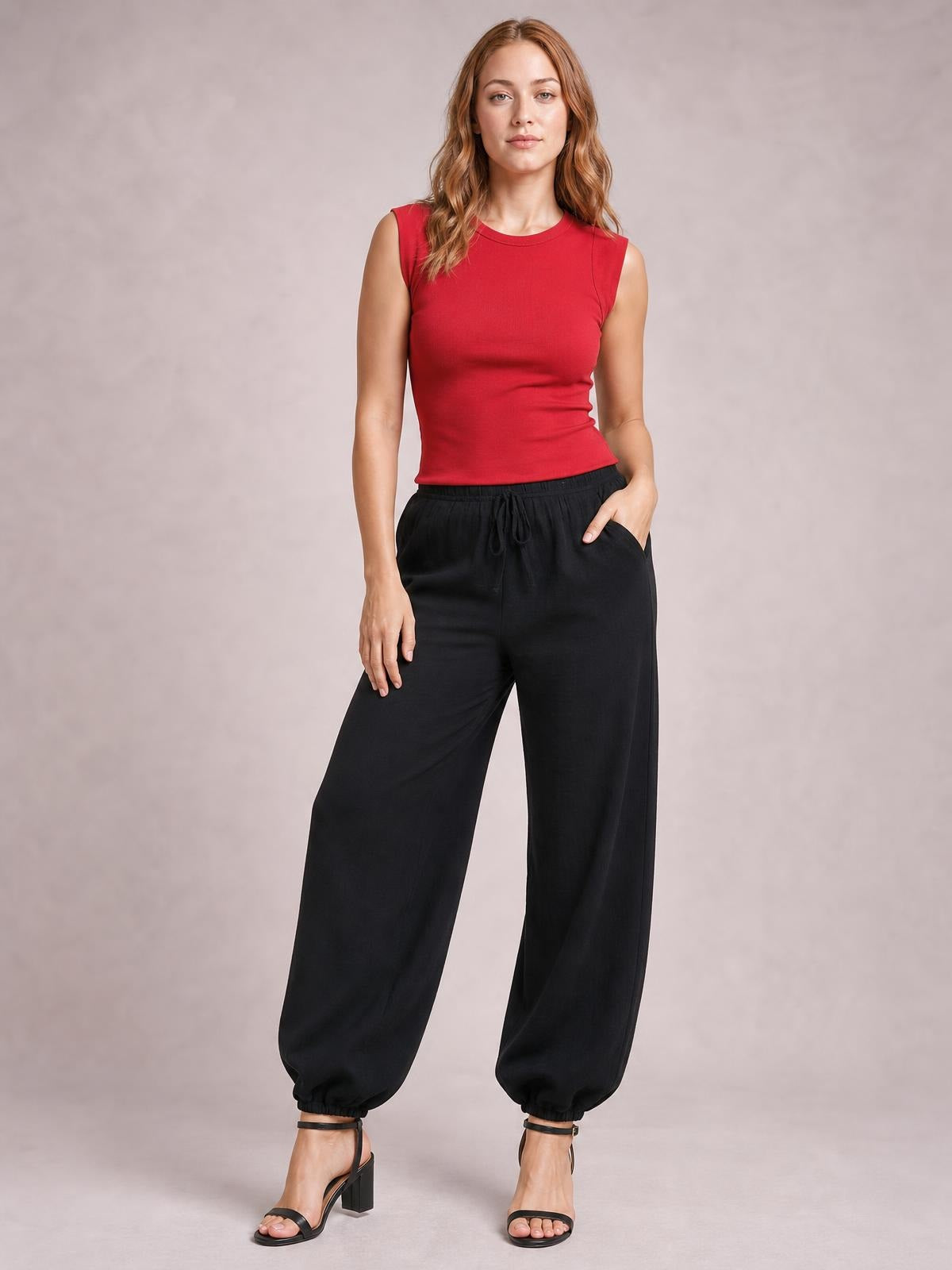 Model wearing black drawstring jogger pants with a relaxed, wide-leg silhouette, elasticized cuffs, and a tied waist, standing with one hand in a pocket.