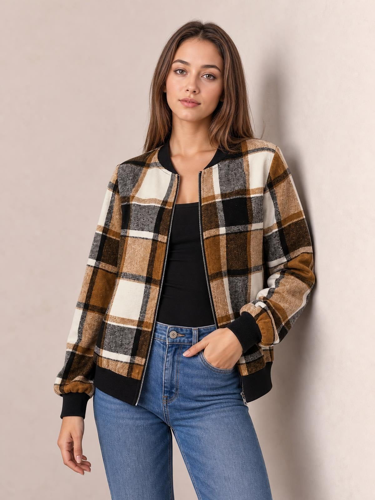 Model wears a brown, black, cream, and gray plaid baseball collar zip-up jacket with ribbed cuffs and hem, posed with one hand in her jeans pocket.