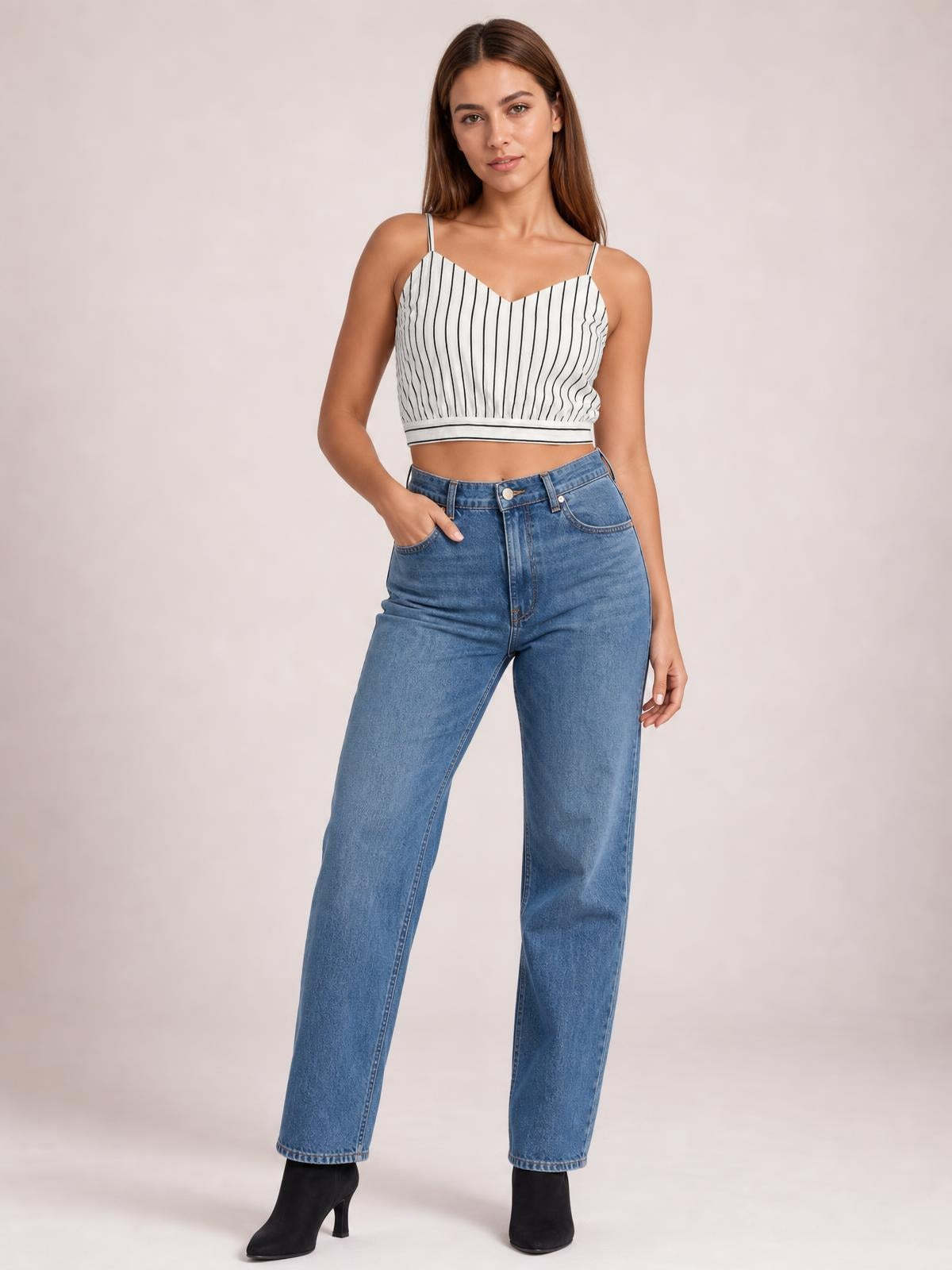 Model poses with one hand in her pocket wearing a white-and-black striped cropped cami with a V-neck, spaghetti straps, and a fitted sleeveless silhouette.