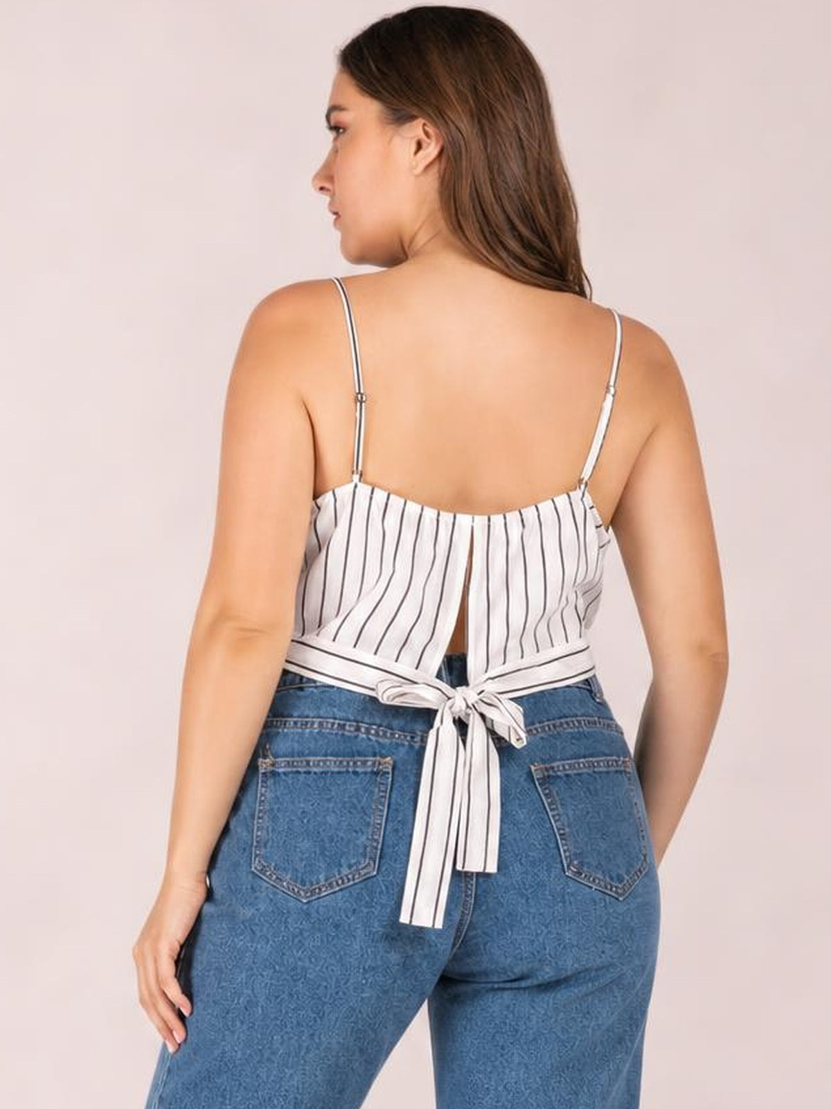 Plus-size model poses in a white striped cropped cami with spaghetti straps, a back tie closure, and a relaxed cropped silhouette.