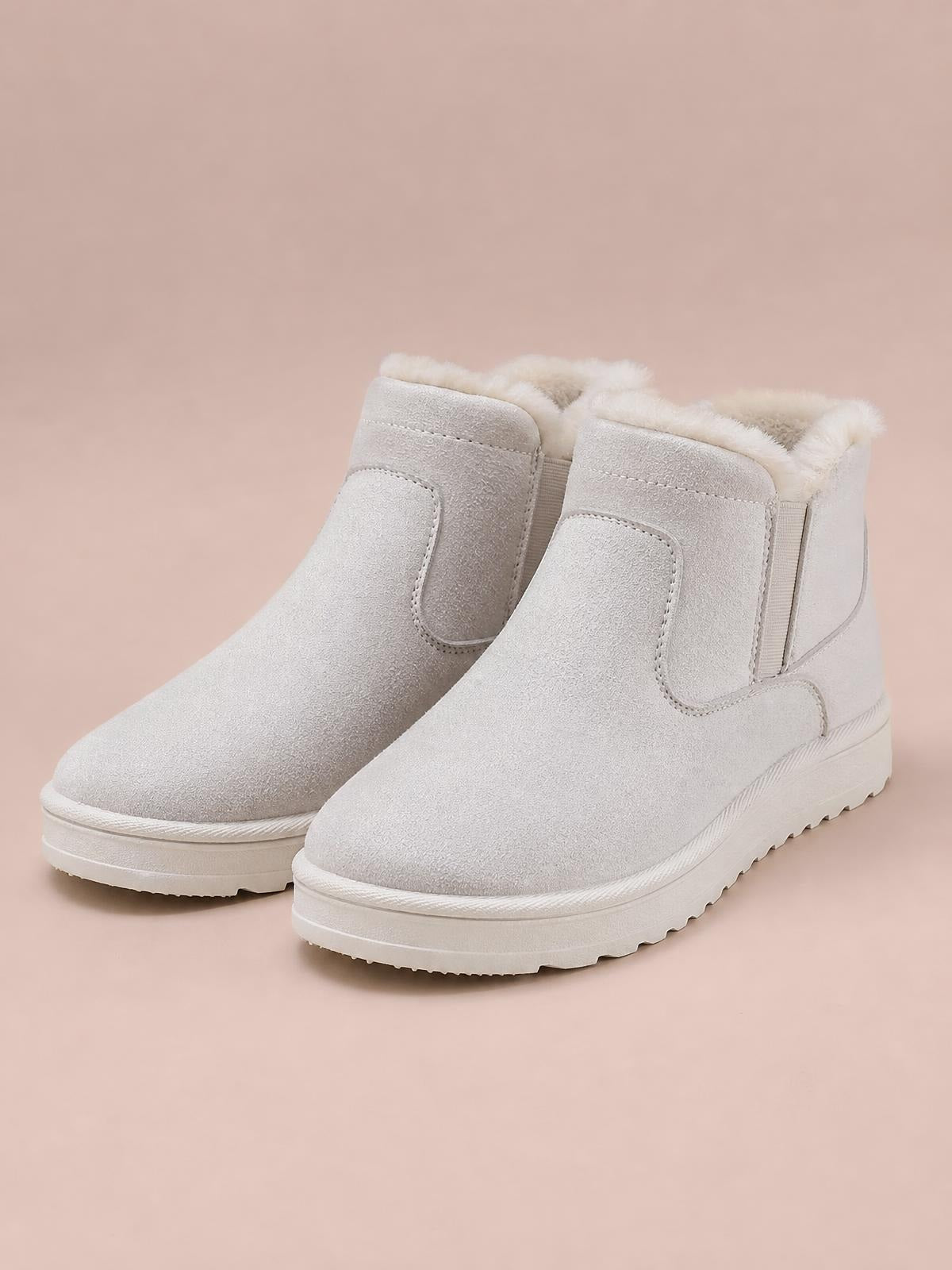Pair of light beige suede ankle boots with plush lining, stitched panel construction, elastic side inserts, flat rubber soles, and rounded toes.