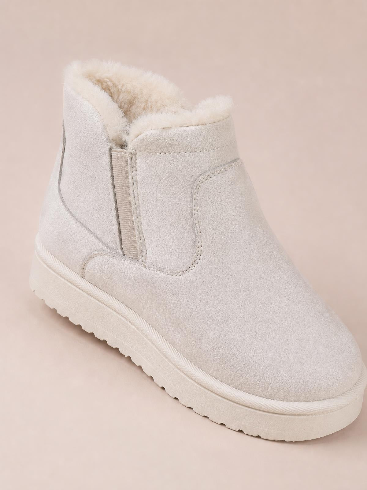 Light beige suede winter ankle boot with plush lining, a flat rubber sole, rounded toe, and stitched panel construction.