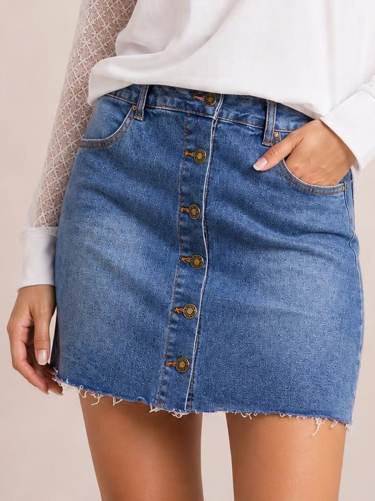 A model wears a blue Pocketed Button Up Denim Skirt with a fitted mini silhouette, front button closure, curved pockets, belt loops, and a frayed hem.
