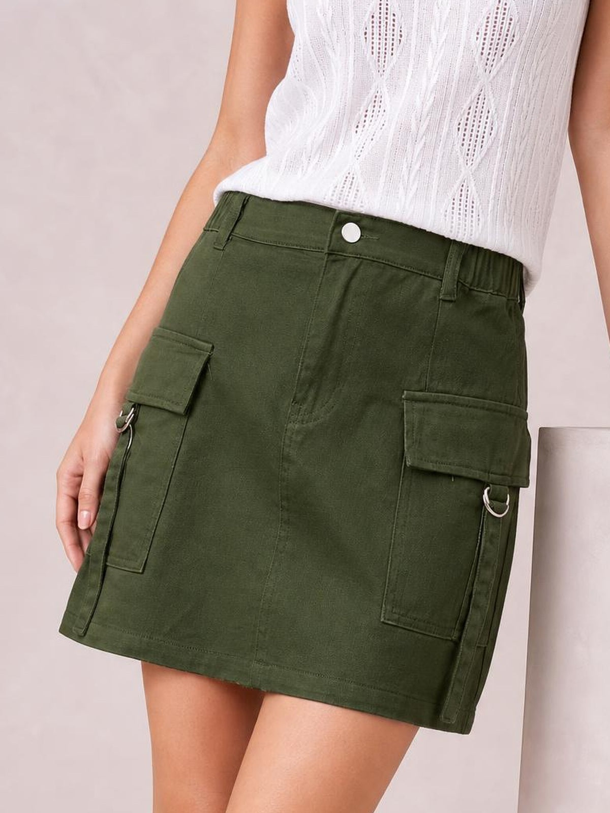 A model wears an olive green Pocketed Buttoned Denim Skirt with a straight mini silhouette, buttoned waistband, flap cargo pockets, and stitched paneling.