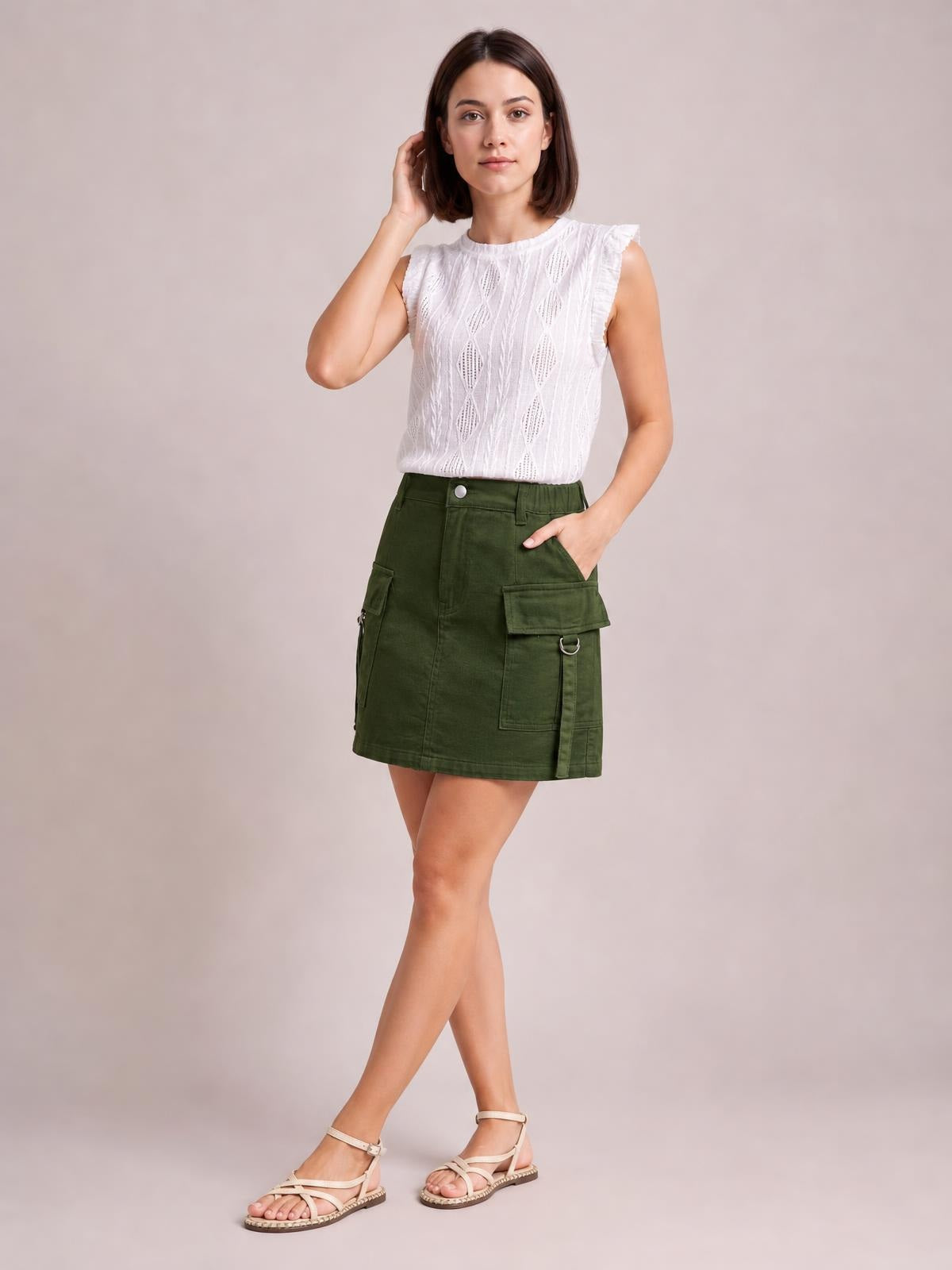 A model poses with one hand in an olive-green pocketed buttoned denim skirt featuring a short straight silhouette, belt loops, and cargo-style pockets.