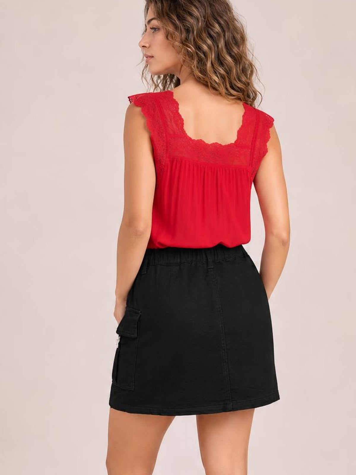 Model poses from behind in a black pocketed denim skirt with a structured waistband, utility side pockets, straight silhouette, and mini-length hem.