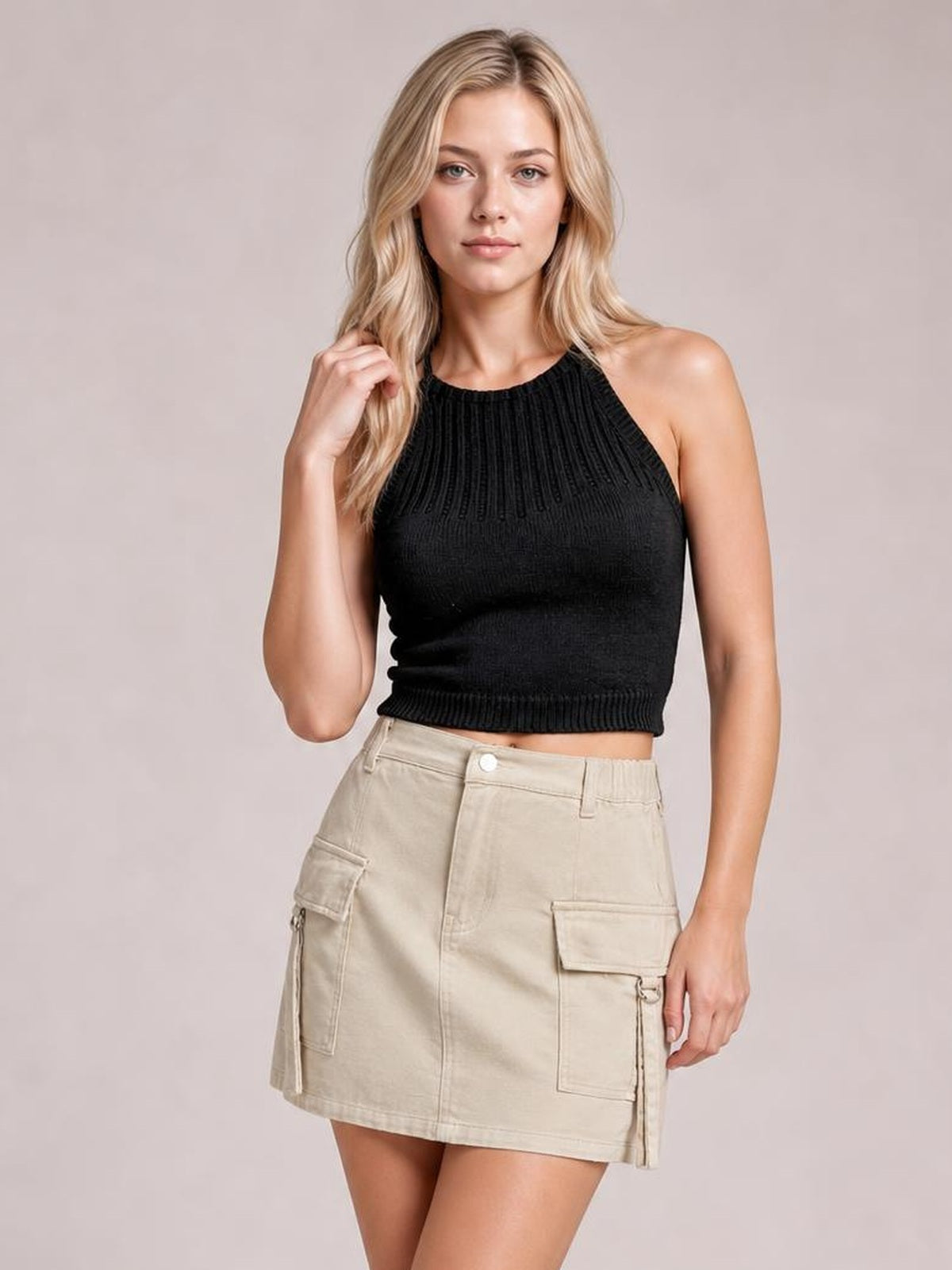 Model wearing a beige pocketed buttoned denim skirt with a high waist, straight mini silhouette, front seam, and flap cargo pockets, posing with one hand in her hair.
